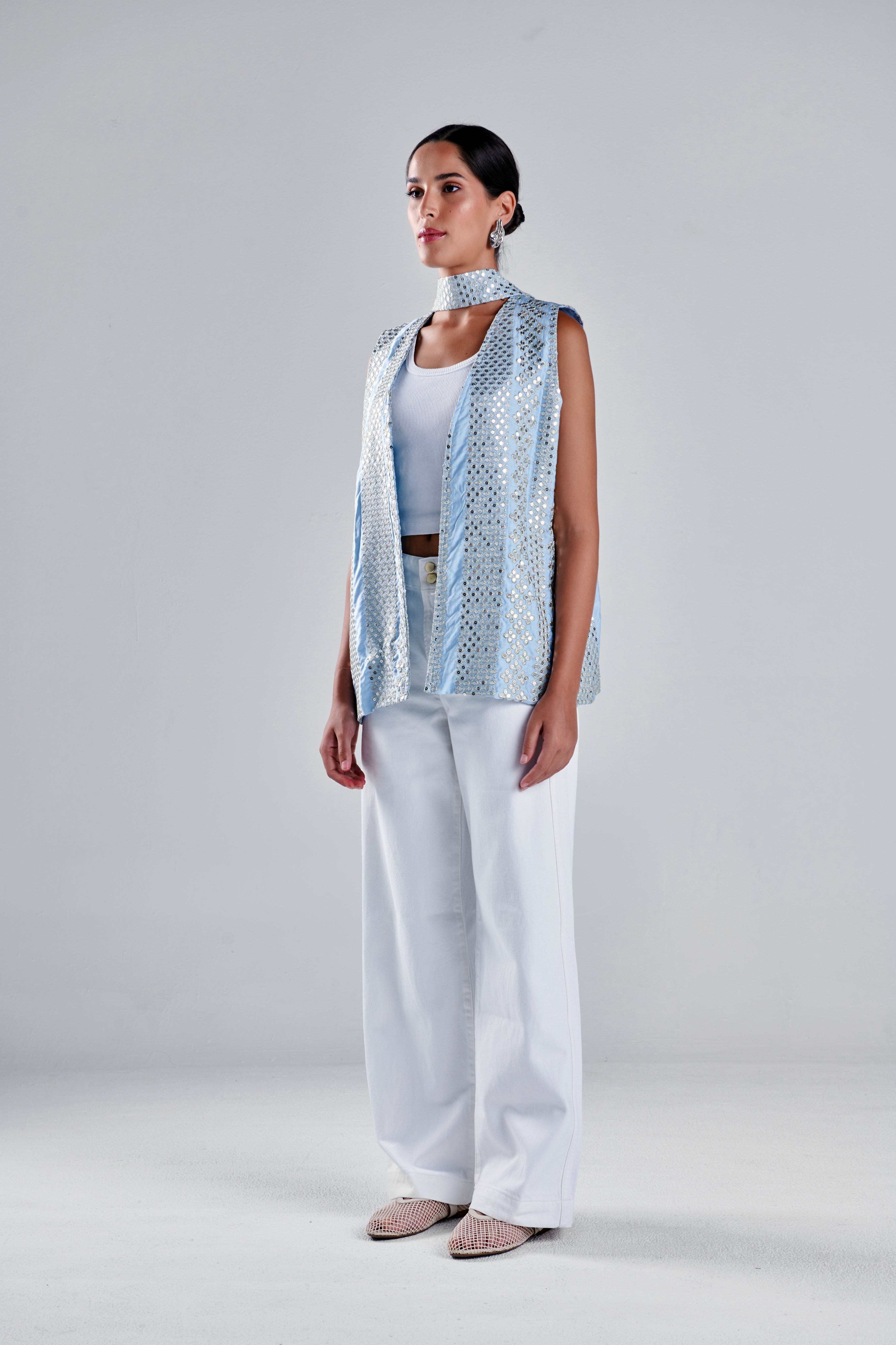 A model stands in a studio wearing a sleeveless light blue patterned vest over a white top and white wide-leg pants, with beige pointed flats. #Baby Blue