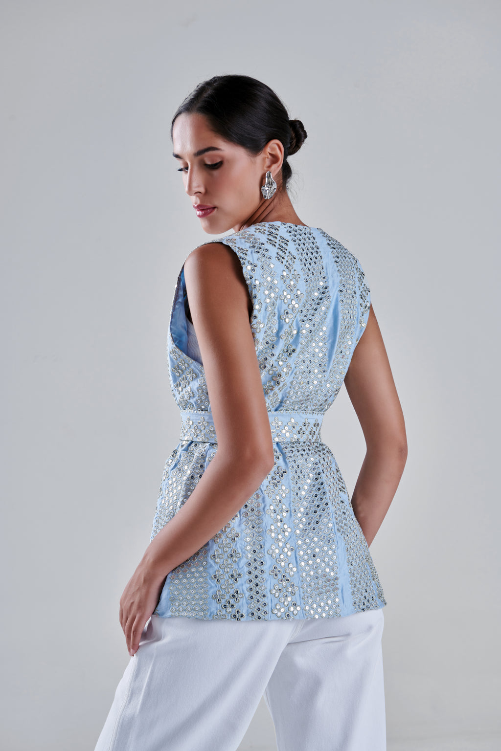 A woman shown from the back wearing a light blue sleeveless top with silver mirror work and white pants, photographed against a plain light gray studio background. #Baby Blue