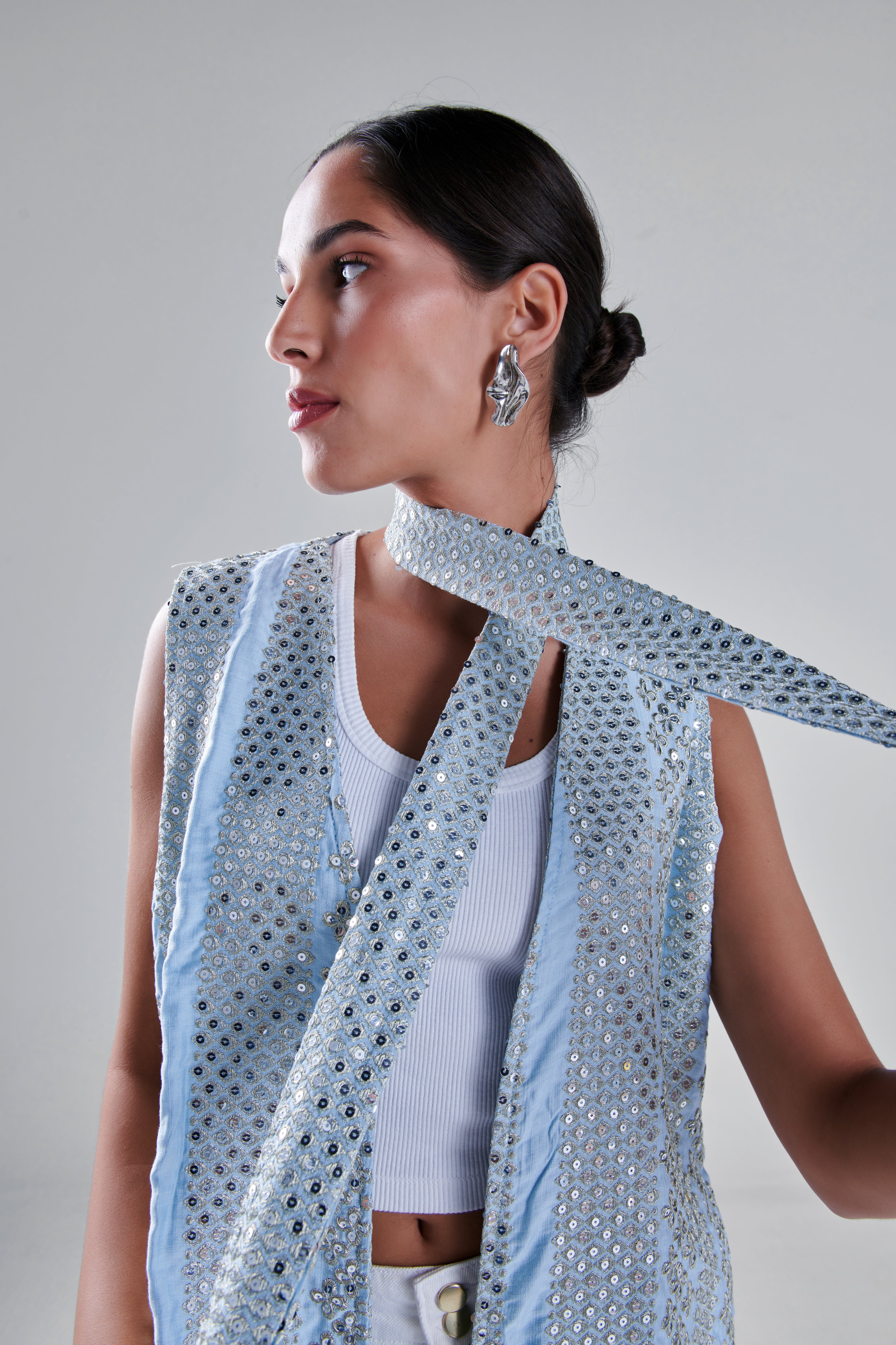A model wearing a light blue sleeveless vest and matching scarf adorned with silver sequins, styled over a white ribbed tank top against a neutral gray background. #Baby Blue
