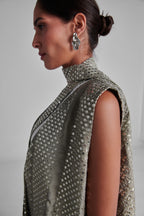 A side-profile view of a model wearing a sleeveless high-neck turtleneck dress covered in shimmering silver sequins, paired with a matching draped scarf and silver statement earrings. #Olive